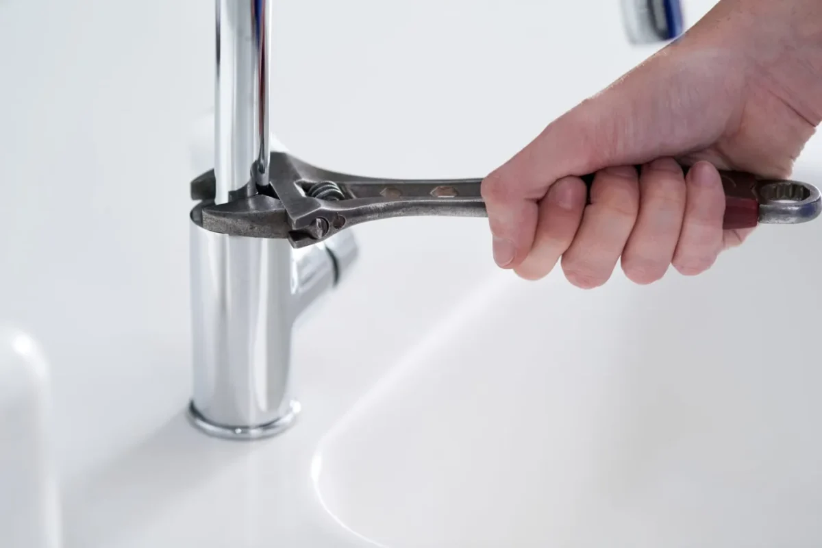 Su tesisatçısı lavabo bataryasını anahtarla onarıyor